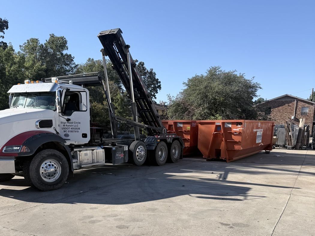 Mack roll-off truck swapping orange containers at a Shreveport commercial site