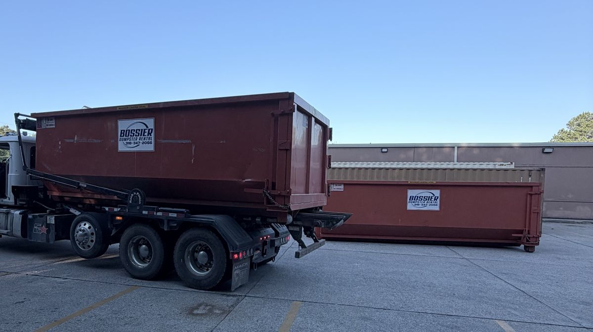 Roll-off truck loading a Bossier Dumpster Rental container behind a retail store