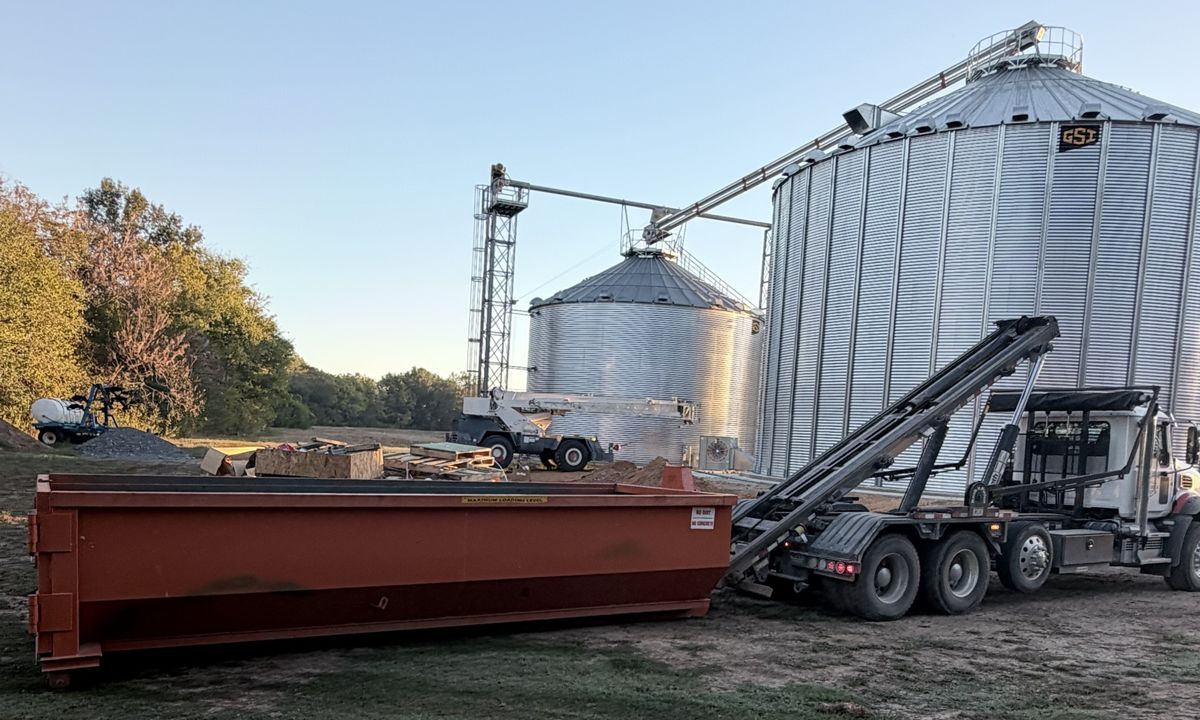 Orange roll-off dumpster on a farm construction site with grain bins